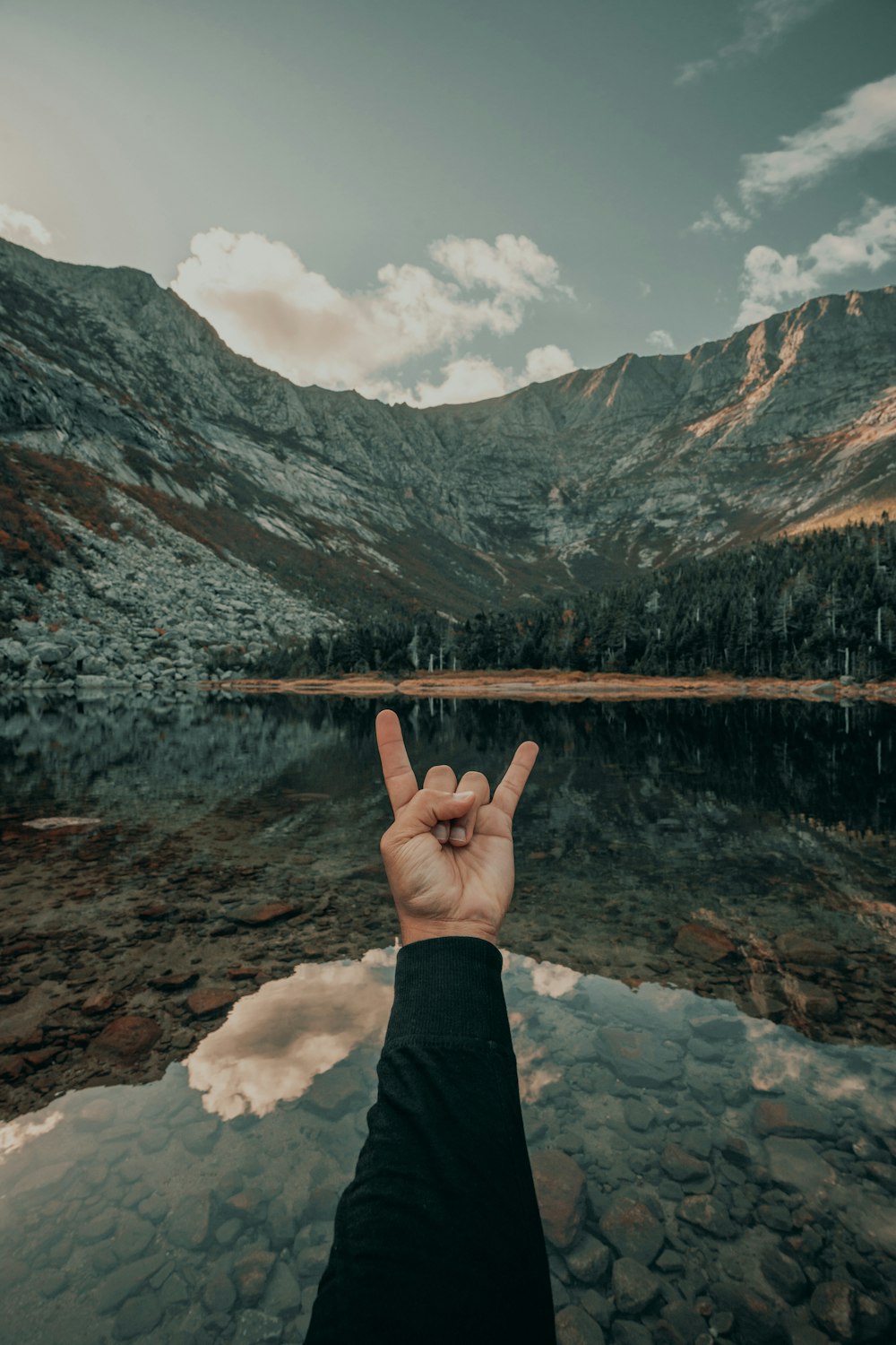 une personne faisant un signe de paix devant un lac de montagne