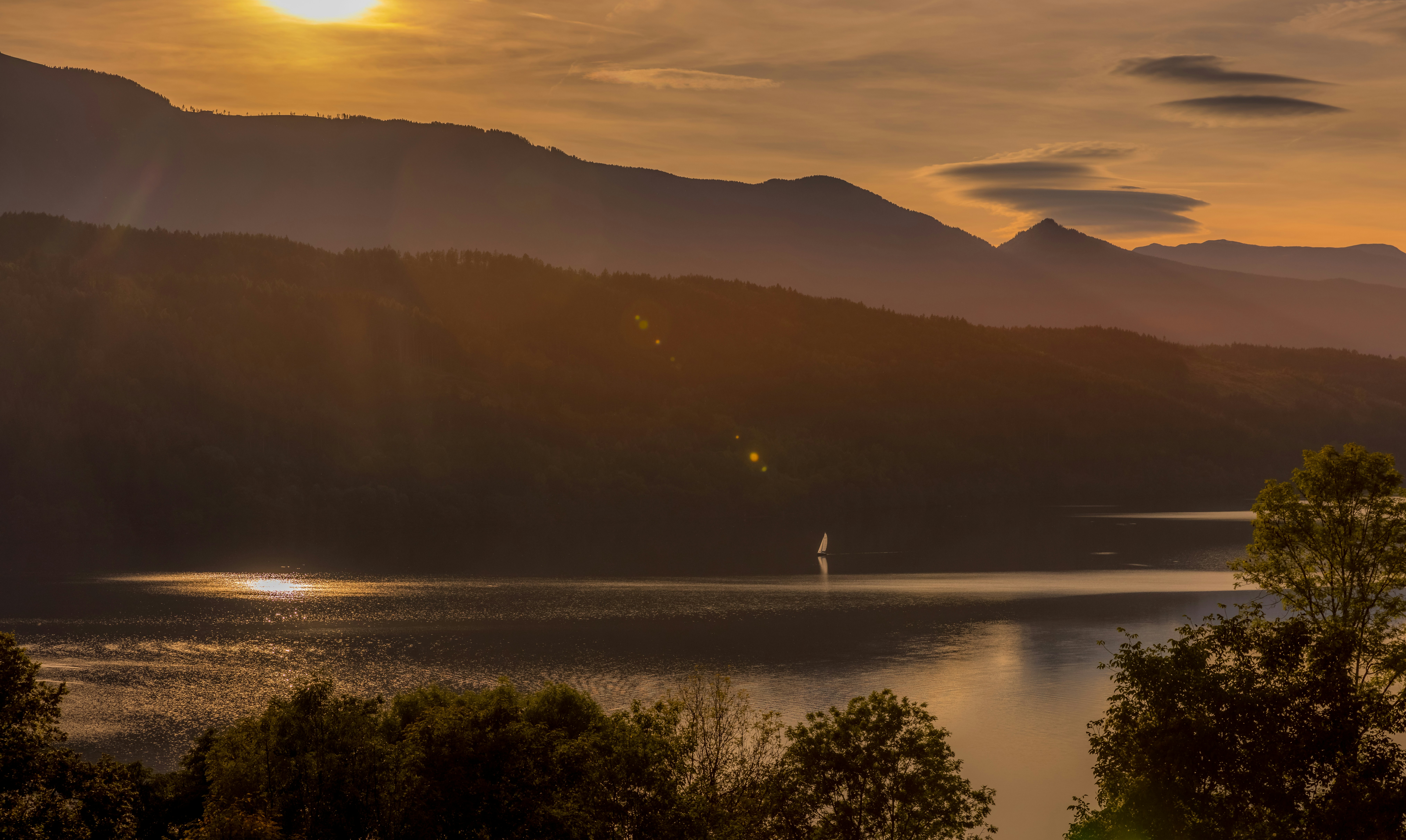 the sun is setting over a lake with mountains in the background