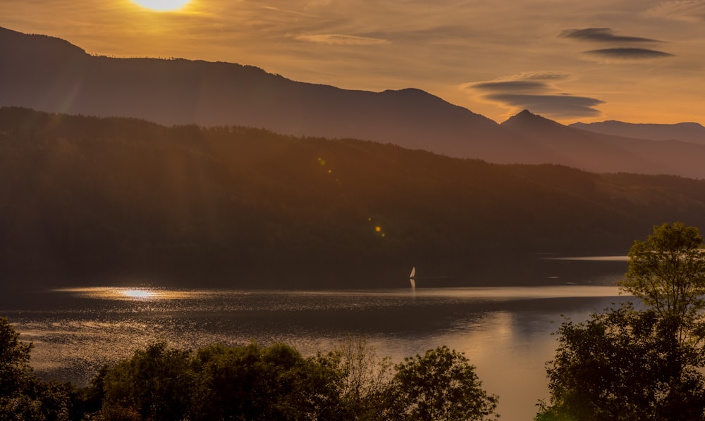 Die Sonne geht über einem See mit Bergen im Hintergrund unter