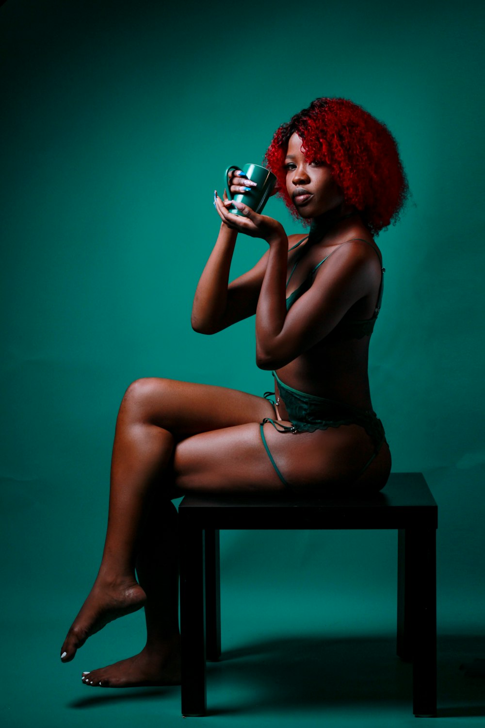 a woman with red hair sitting on a stool holding a cup
