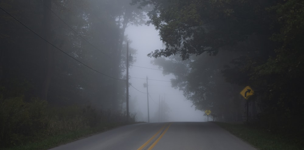 a foggy road with a yellow sign on the side