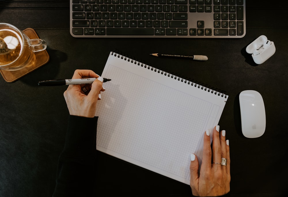 a person writing on a notebook next to a keyboard