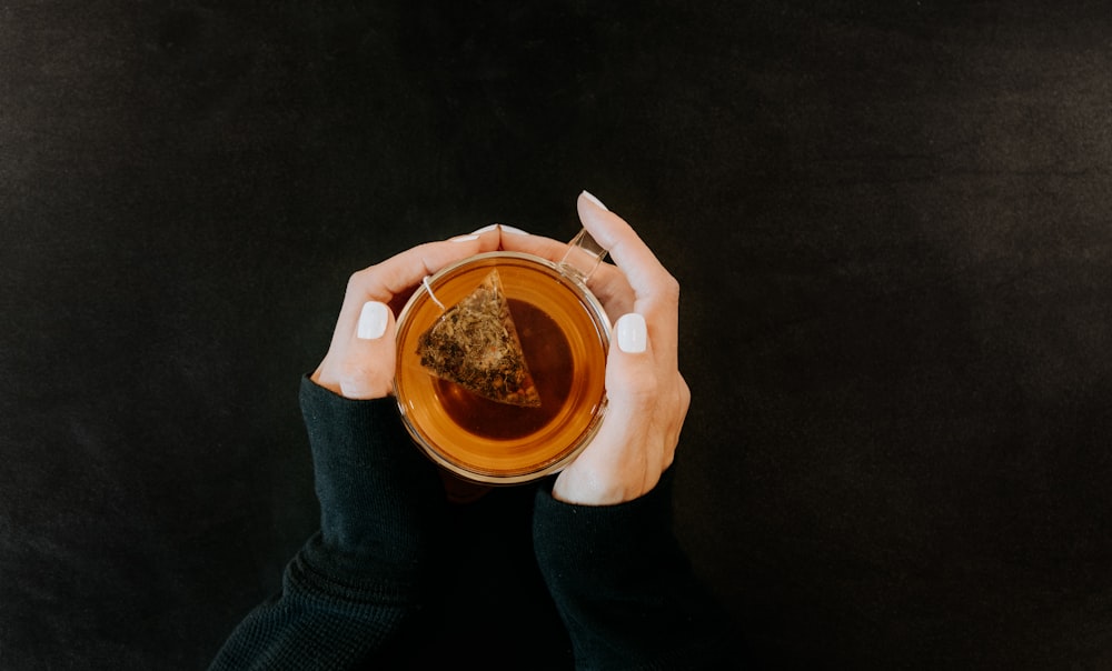 a woman holding a cup of tea with a piece of cake on top of it