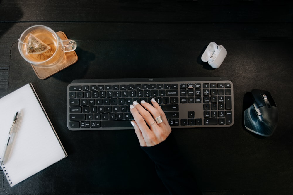 a person typing on a keyboard next to a cup of coffee