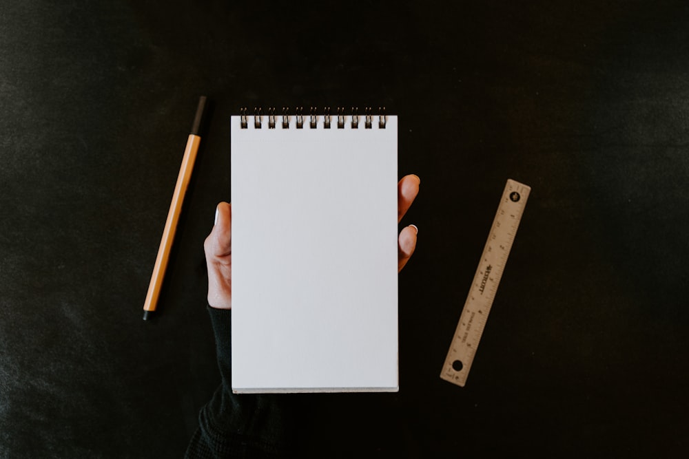 a person holding a notebook with a pencil next to it