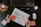 On a dark table, there's a keyboard and mouse, a notebook with a flowchart sketch labeled 'User Flow,' a hand holding a marker writing on a sticky note, a pencil, AirPods, and a glass of tea with a teabag.