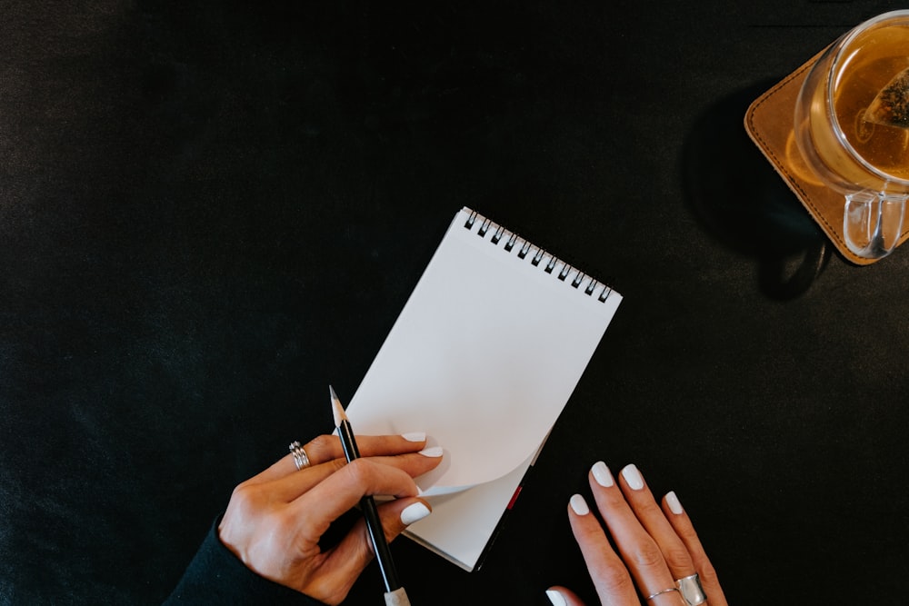 a woman writing on a notepad next to a cup of coffee