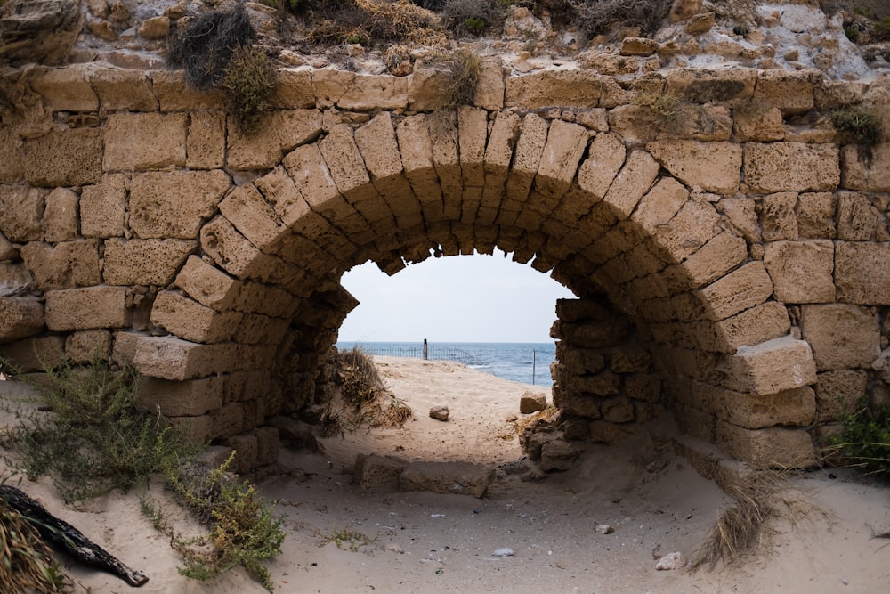 Un túnel de piedra en una playa de arena con el océano al fondo