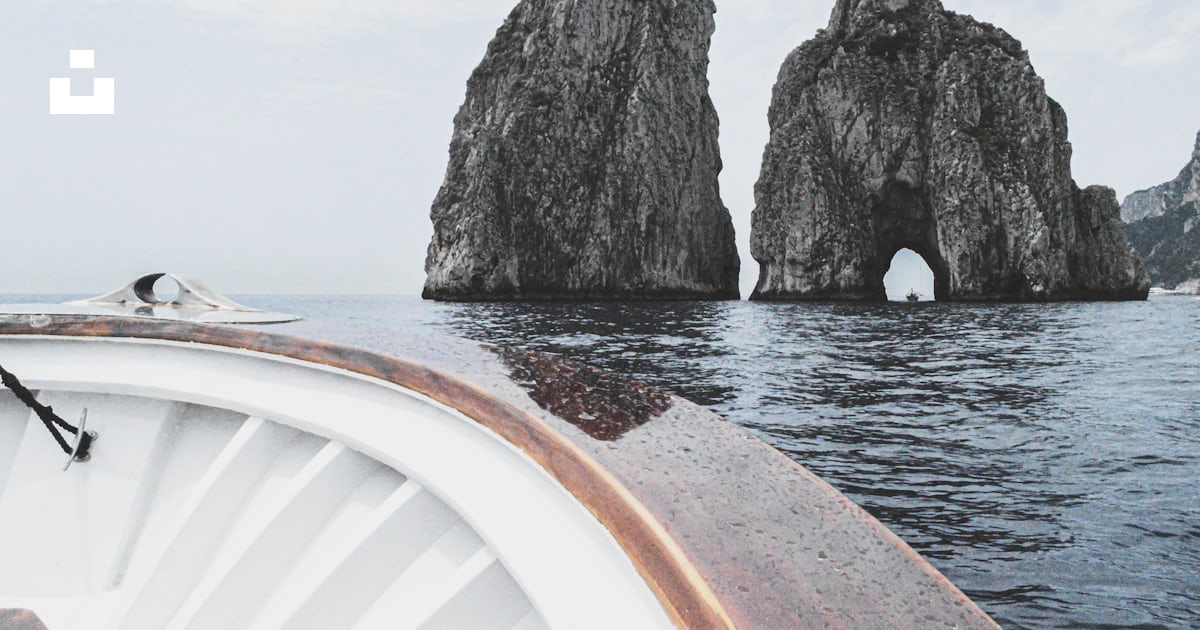 A boat traveling past two large rocks in the ocean photo – Free Italy ...