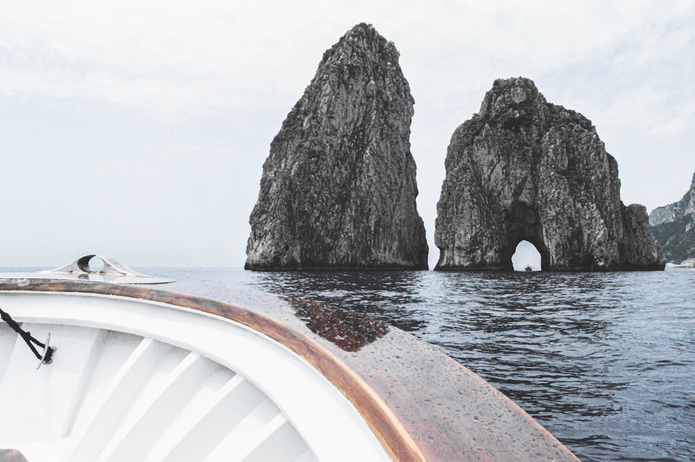 a boat traveling past two large rocks in the ocean