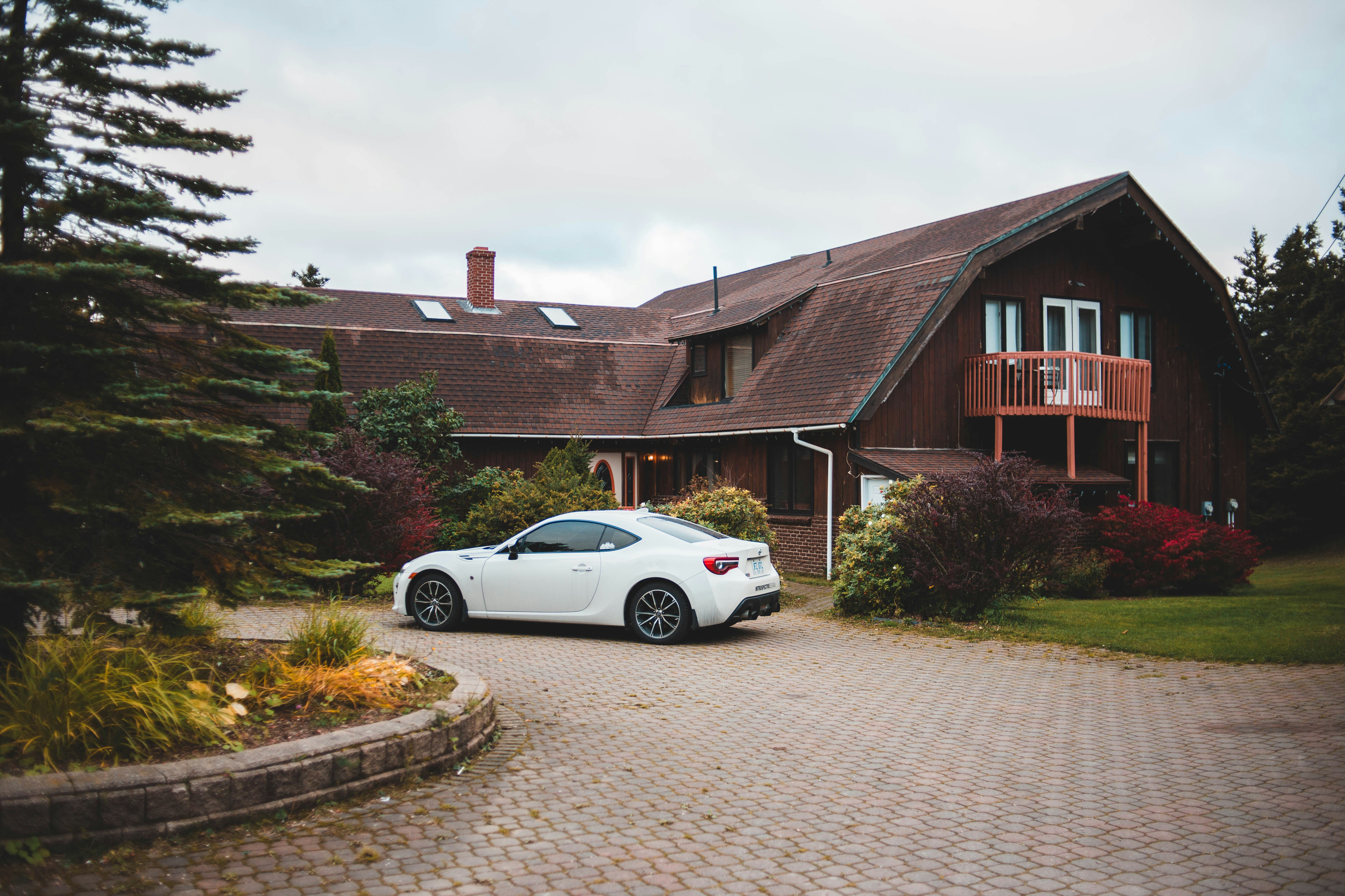 A white car parked in the paved driveway of a wooded home under a cloudy sky &mdash; what a car rental delivered to your home in New Hampshire looks like on arrival