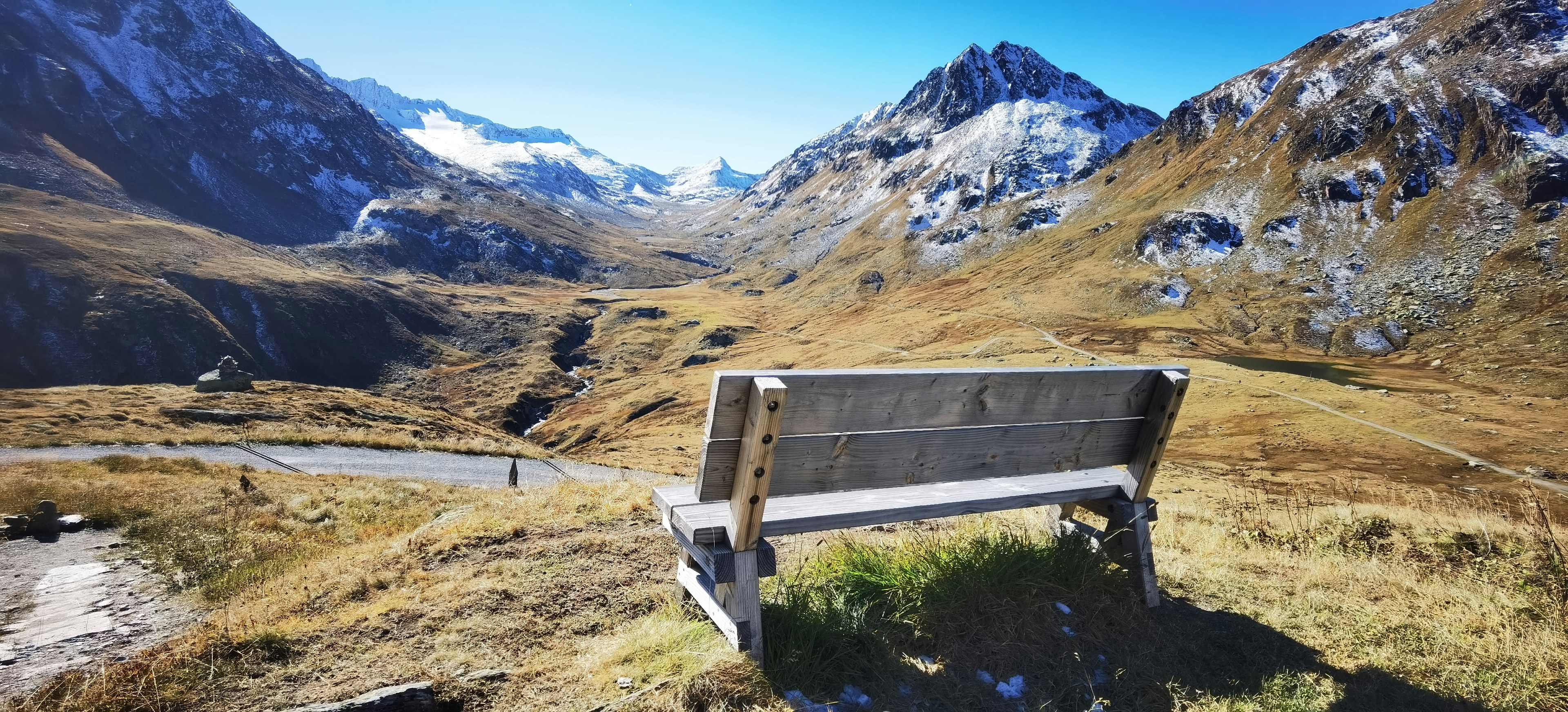 a wooden bench sitting on top of a grass covered hillside | Houfy — Book Direct