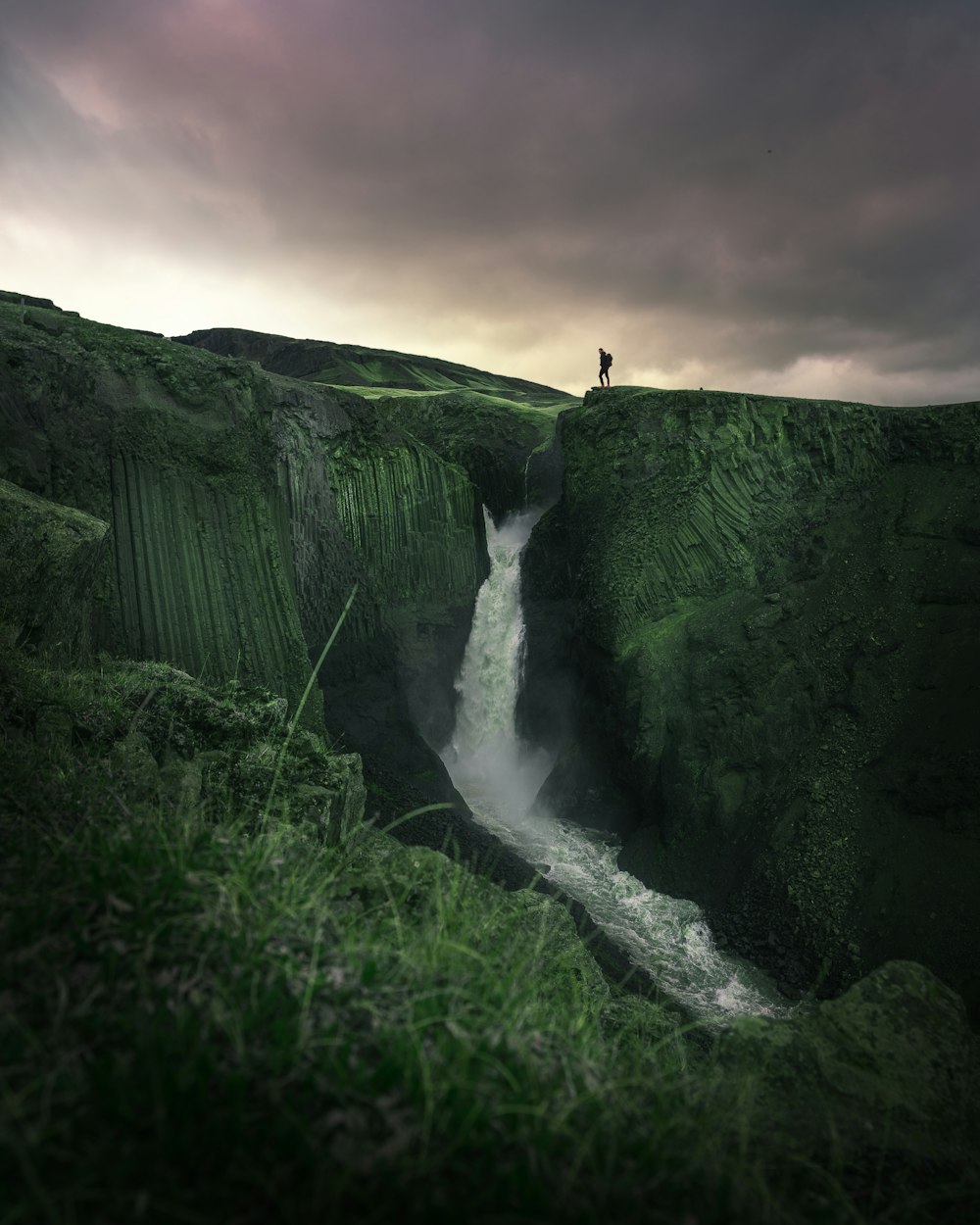 a man standing on top of a cliff next to a waterfall