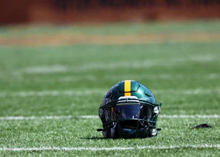 Close-up of a football helmet resting on the grass with the Methacton logo clearly visible.