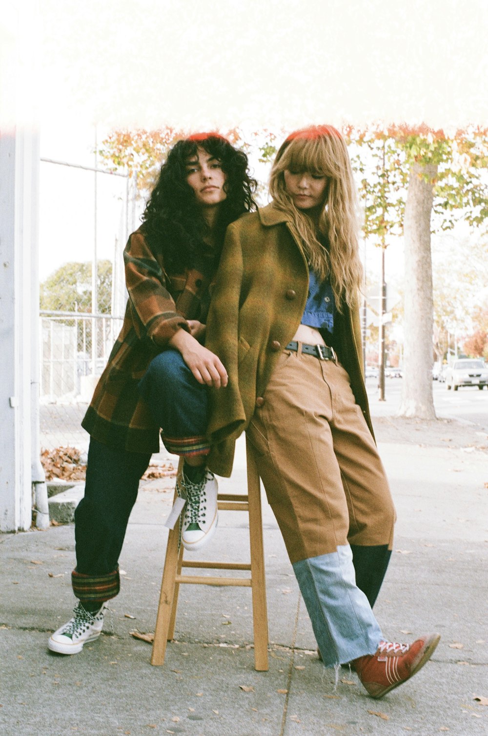 two young women sitting on a stool in front of a building