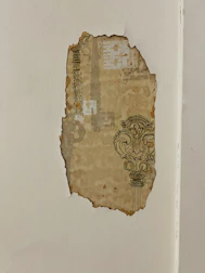 A close-up of hands carefully removing old wallpaper to prepare a wall for a fresh finish.