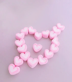 A collection of small collectible squishies arranged in a heart shape on a white background with subtle pastel stars.