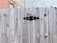 A wooden fence with a prominent black hinge, set against a background of a brick and stone building.