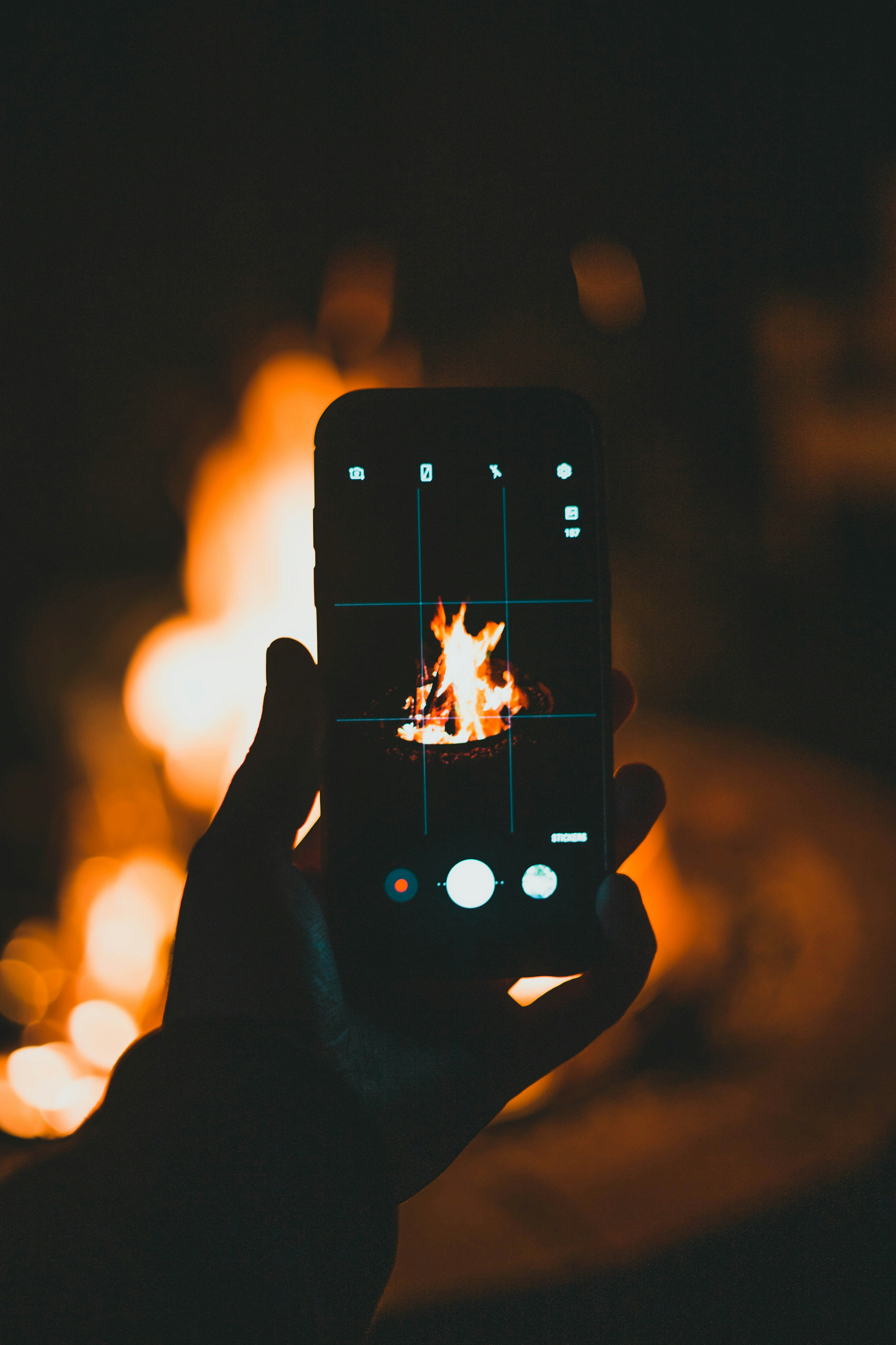 a person holding a cell phone in front of a fire