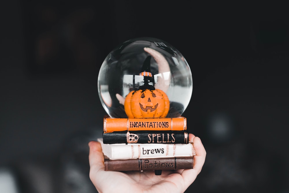 a hand holding a snow globe with a pumpkin inside of it