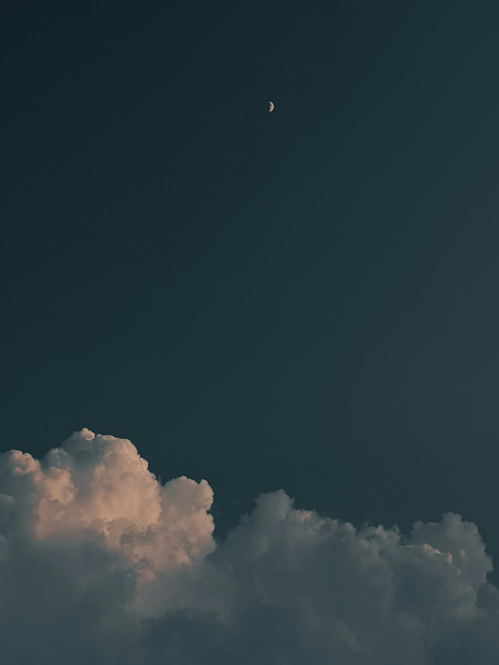 a plane flying through a cloudy sky with a moon in the distance