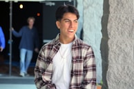A candid photo of a young man in a casual shirt, standing outdoors with a friendly smile.