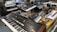 A variety of electronic musical keyboards and synthesizers arranged on a tabletop and stands, including models with an array of dials, switches, and sliders. The setup appears to be in a studio or showroom setting.