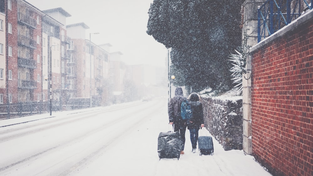 a couple of people walking down a snow covered street