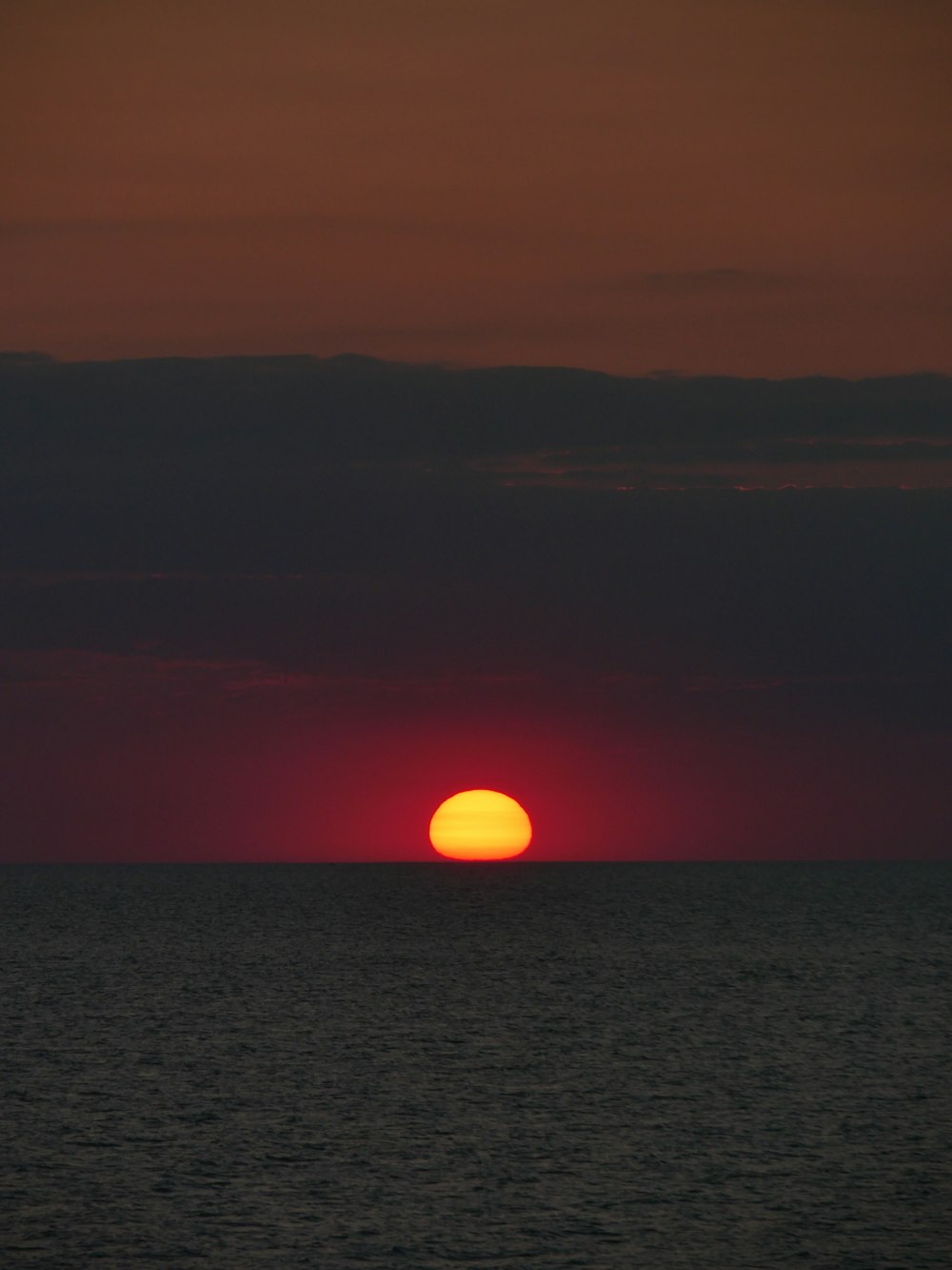 the sun is setting over the ocean on a cloudy day