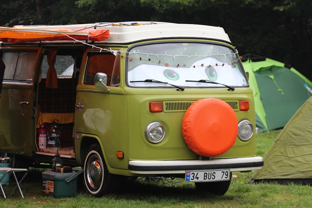 a green vw bus parked in a field next to a tent