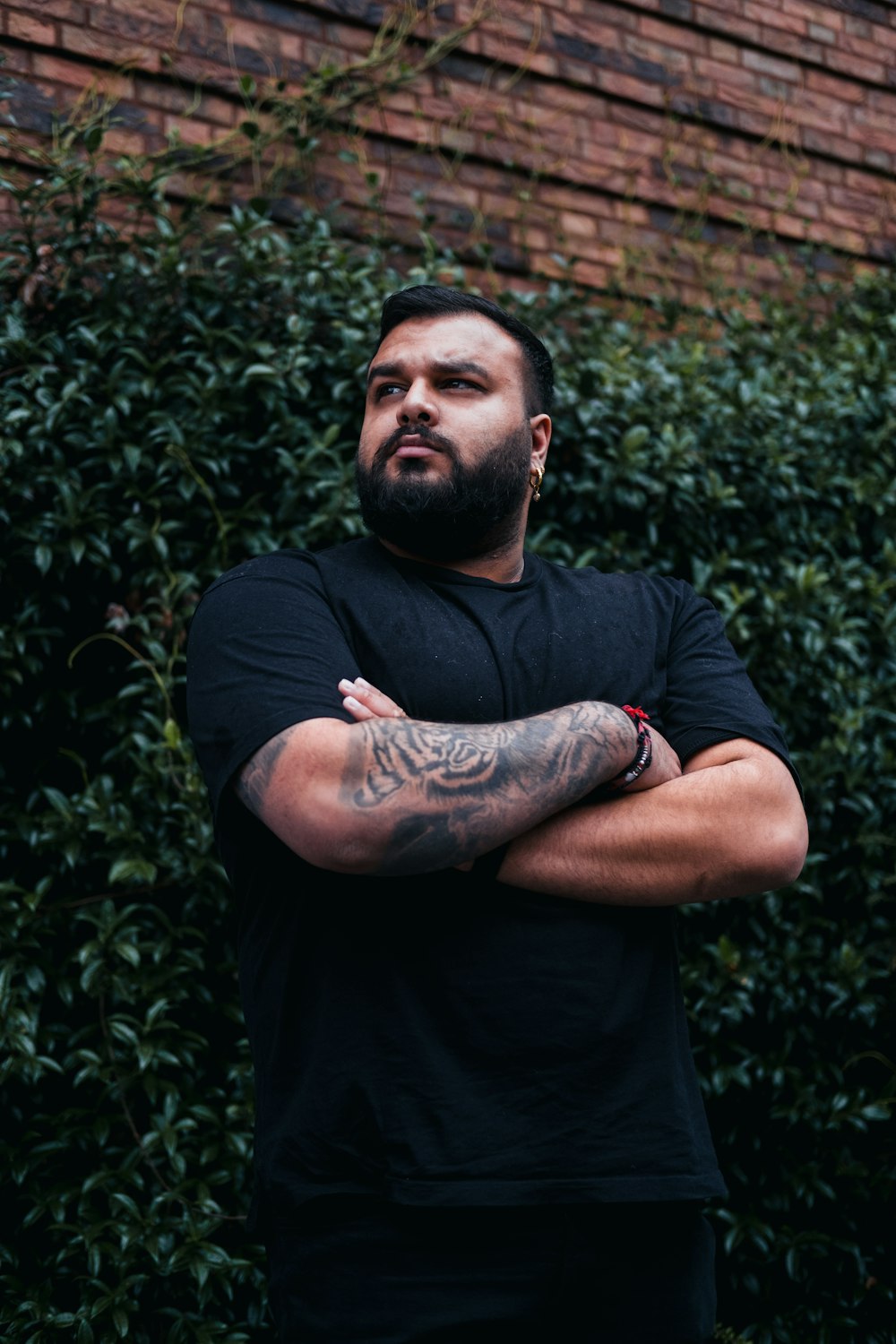 a man with his arms crossed standing in front of a brick wall