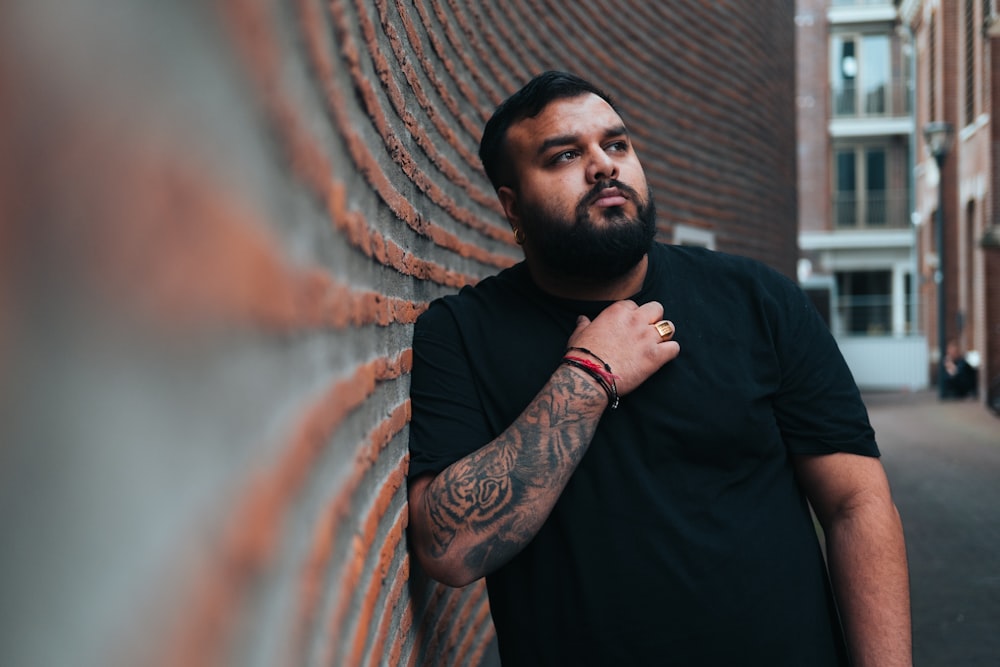 a man with a tattoo on his arm leaning against a brick wall