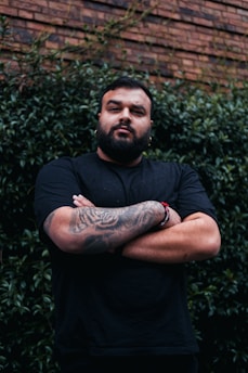 a man with tattoos standing in front of a brick wall