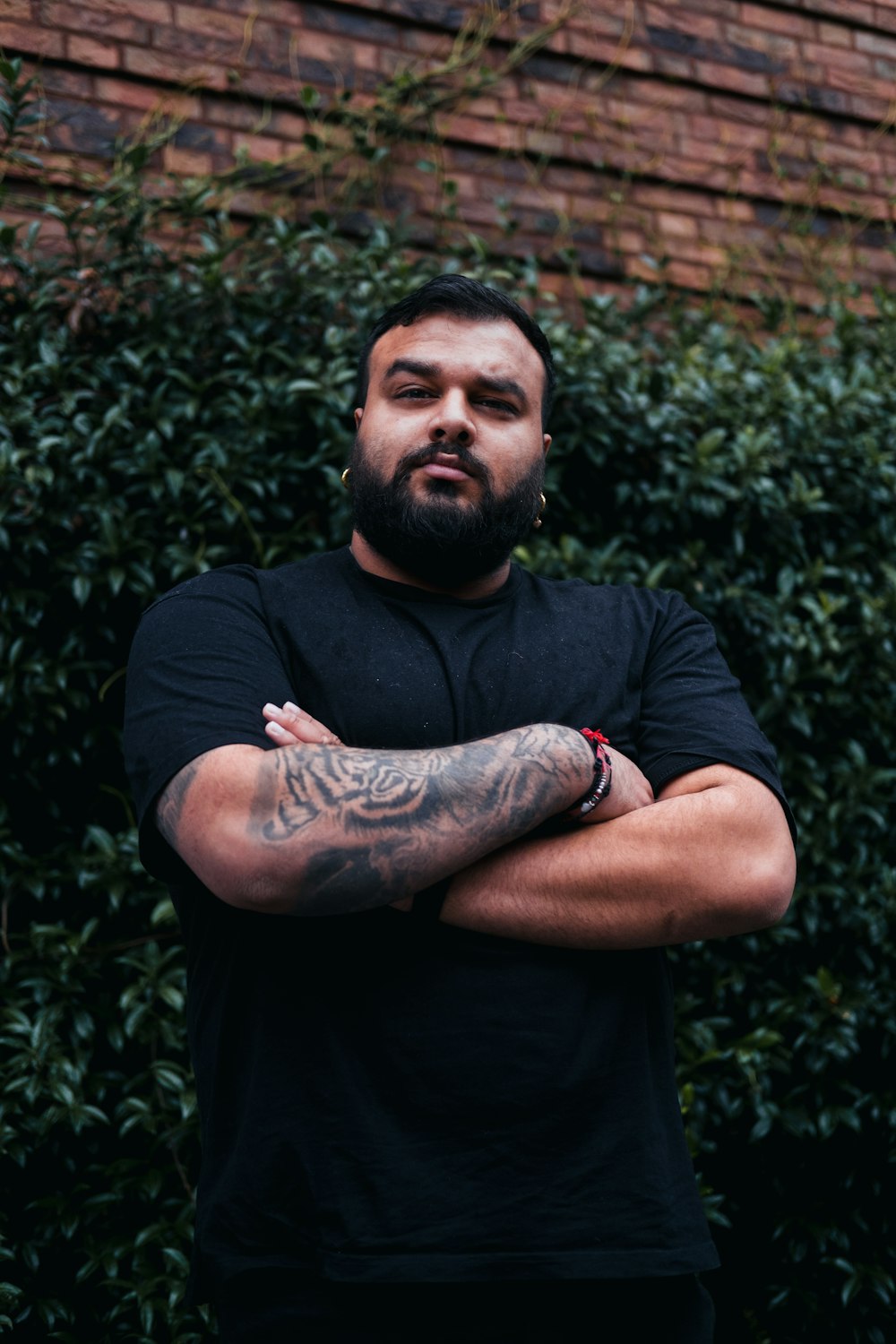 a man with tattoos standing in front of a brick wall