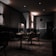 A dimly lit cafe or restaurant interior with a modern design. The room features several tables and wicker chairs, with glass partitions placed between the tables. The walls are decorated with minimalist artwork and warm lighting fixtures. The overall ambiance appears quiet and intimate.
