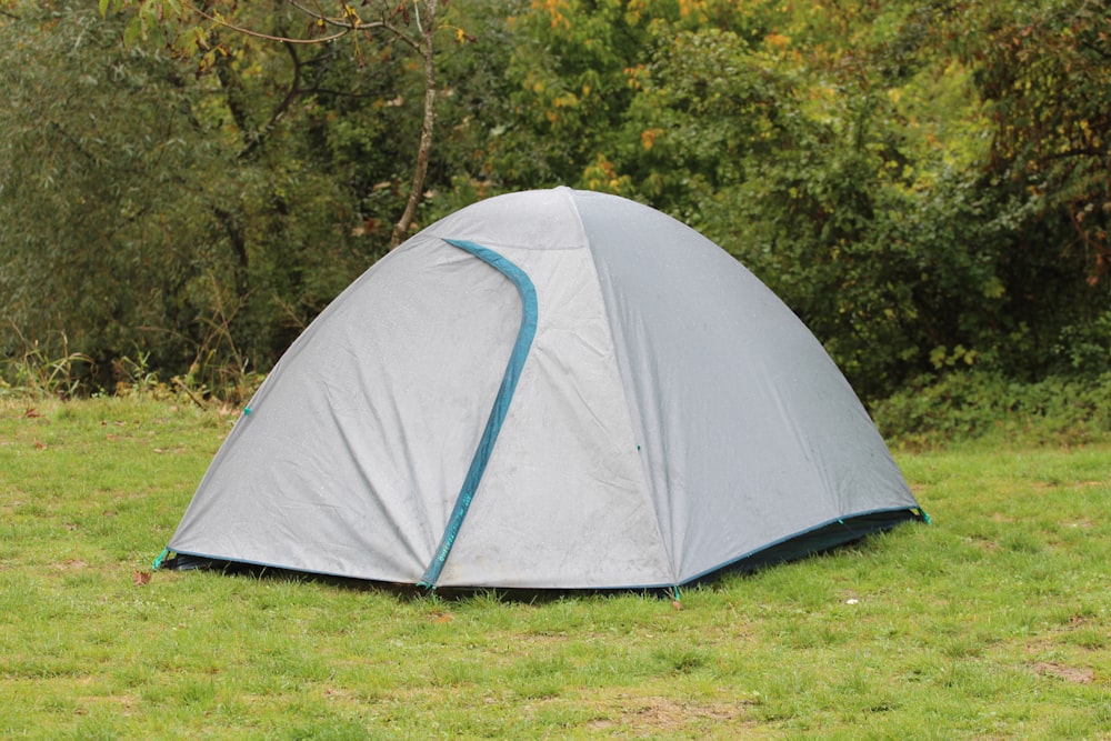 a tent pitched up in a field with trees in the background