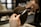 A hairdresser carefully trims a person's short, brown hair using scissors and a comb. The focus is on the precise cutting technique as the hands hold the tools expertly.