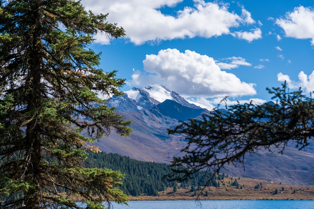 a lake surrounded by mountains and trees under a cloudy blue sky