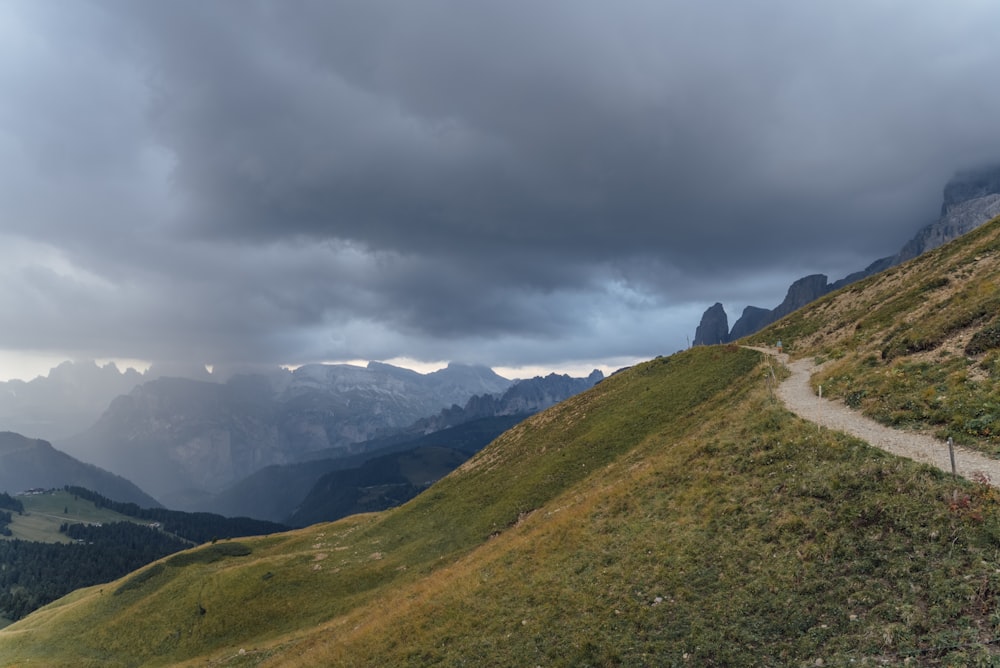 a dirt road on a grassy hill with mountains in the background