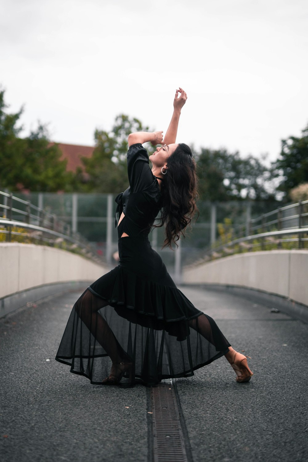 a woman in a black dress dancing on a bridge