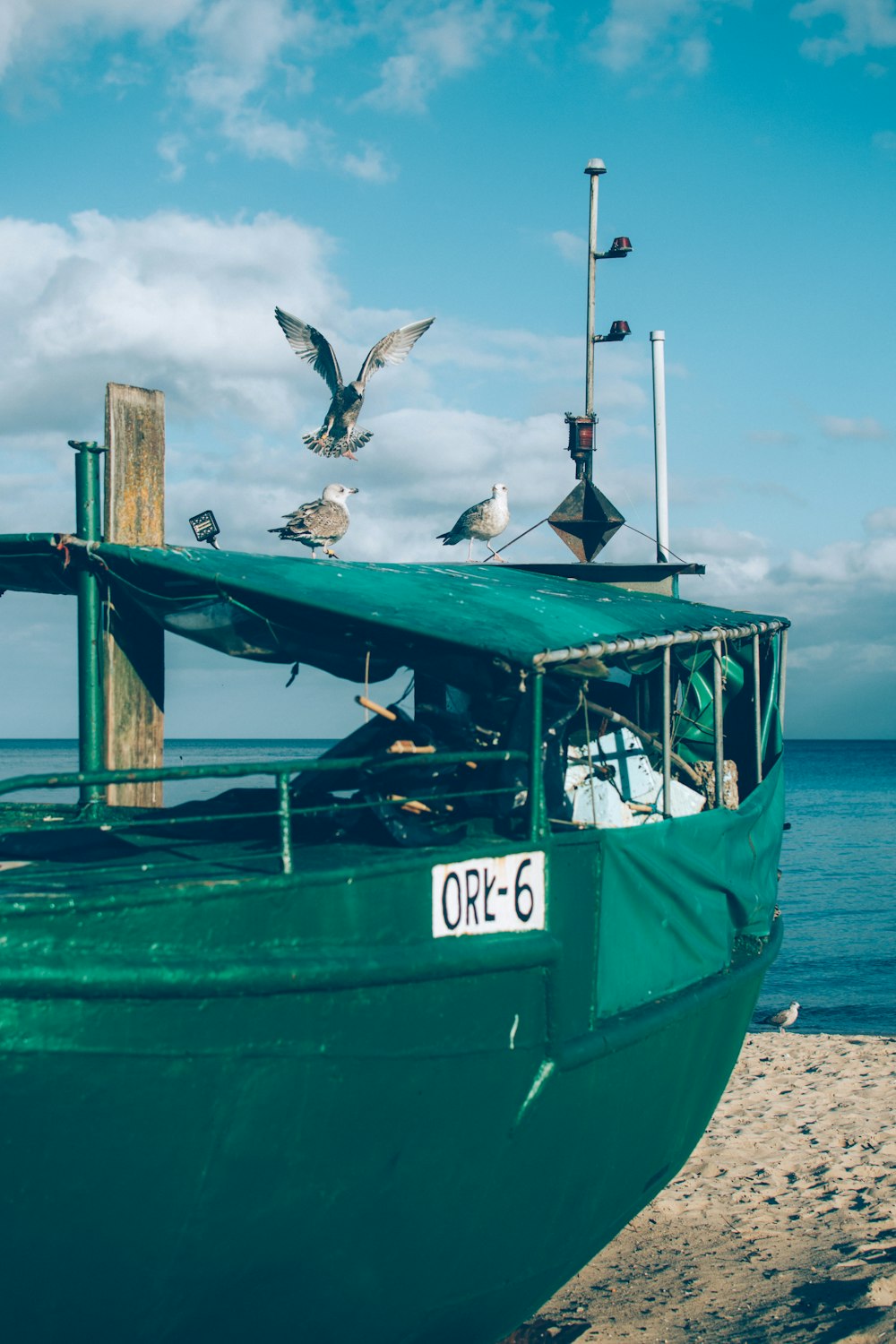 a green boat sitting on top of a sandy beach