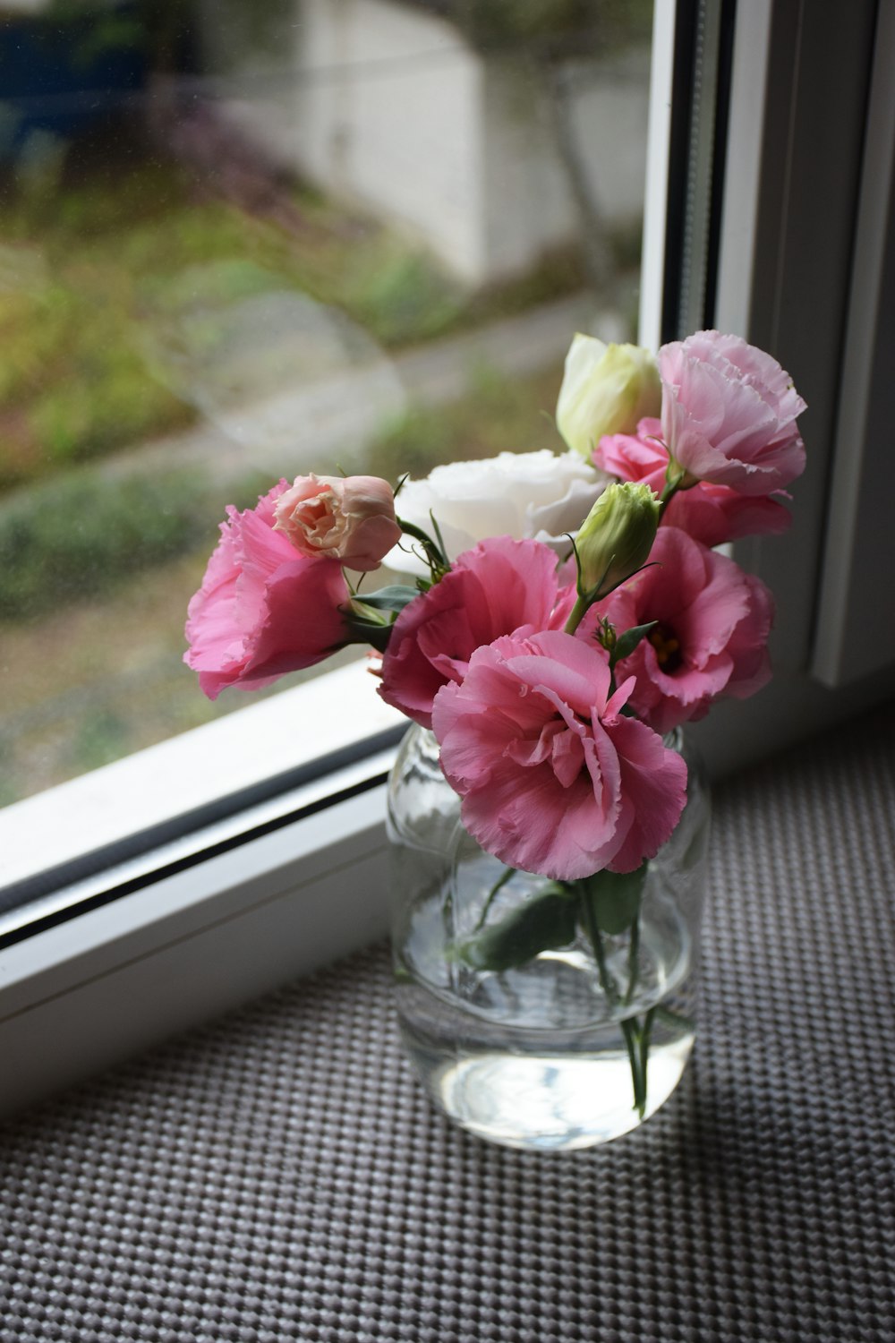 a vase with pink and white flowers on a window sill