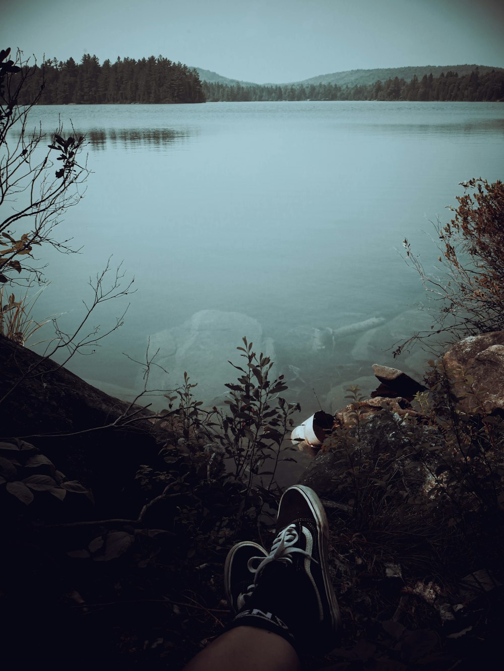 a person's feet resting on a rock near a lake