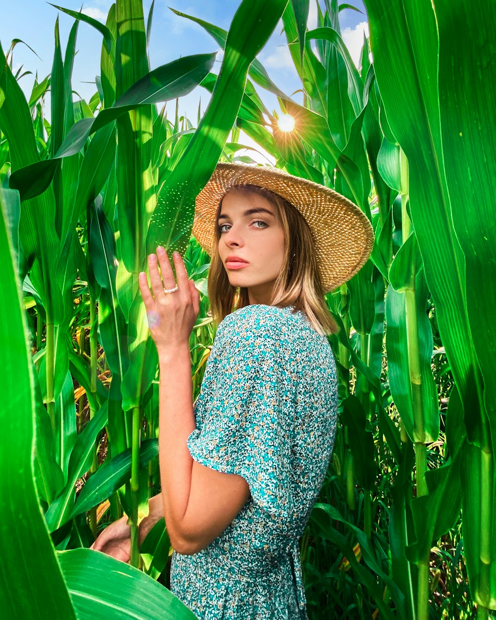 a woman wearing a straw hat standing in a corn field