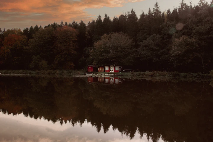 A small red camp and boats on a quiet Muskoka-area lake at dusk