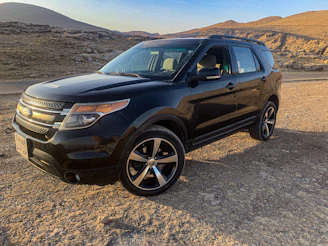 A sleek armored SUV parked against a backdrop of the Andes mountains at dusk, under a moody sky.