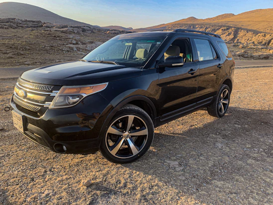 A sleek armored SUV parked against a backdrop of the Andes mountains at dusk, under a moody sky.