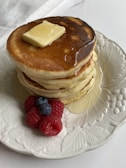 A plate of golden-brown pancakes topped with fresh berries and a drizzle of maple syrup.