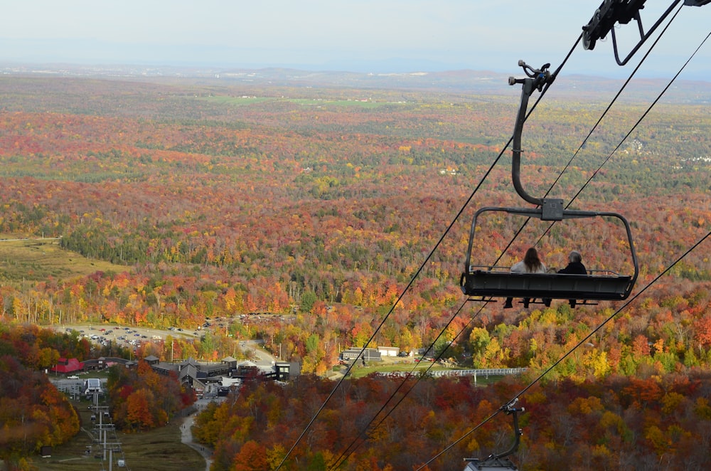 a couple of people riding a ski lift over a forest