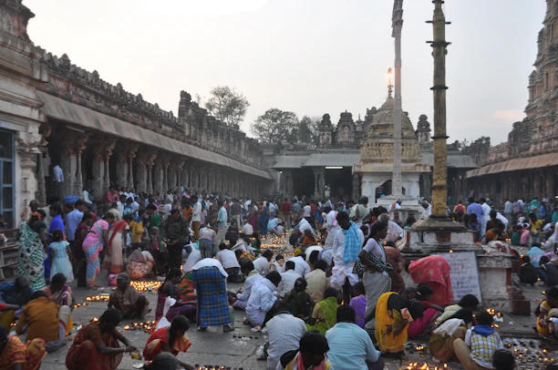 A vibrant scene of devotees lighting diya lamps during a colorful Hindu festival at a temple courtyard.